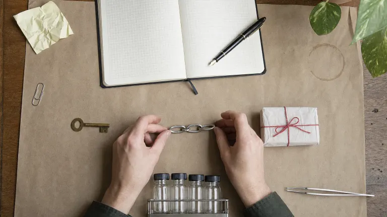 Overhead view of a key, a short chain and a small wrapped parcel in a line, with vials and a notebook.